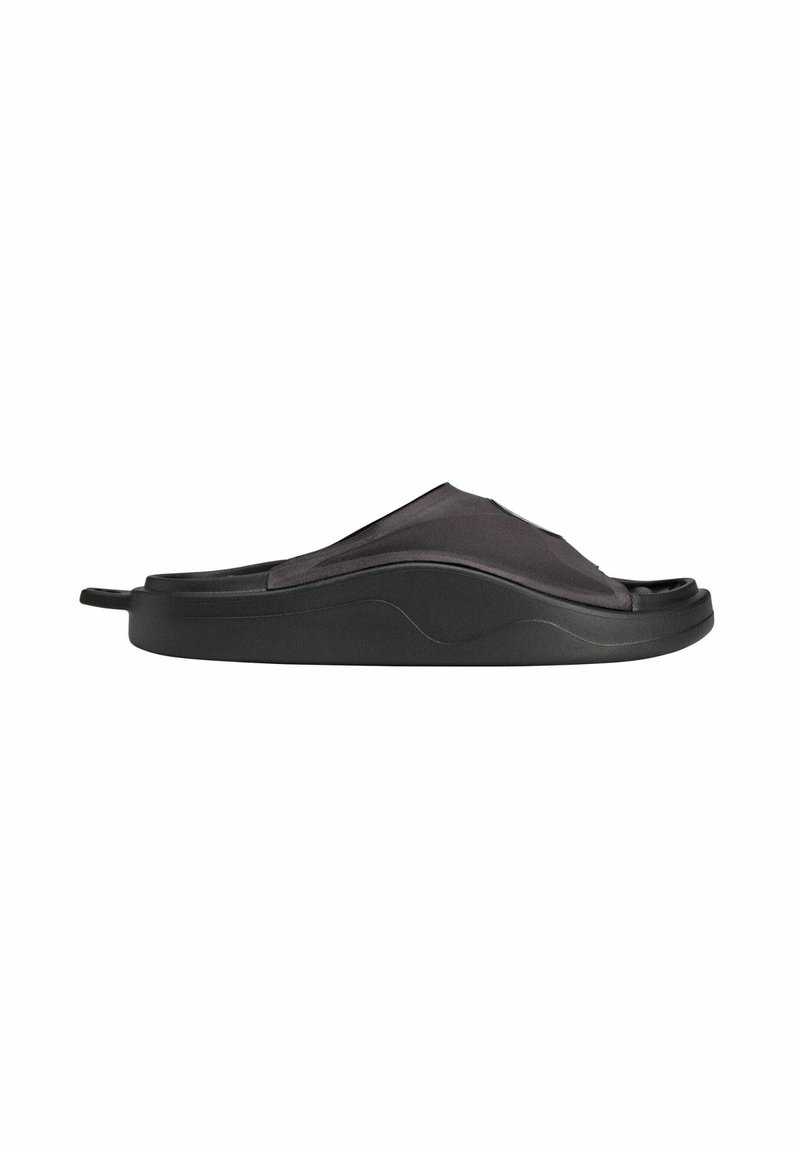 Svart slip-on sandal i en slät, böjd design; tillverkad av flexibelt material; har en texturerad ovansida och en stödjande sula.