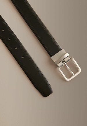 Čierny kožený opasok so striebornou obdĺžnikovou prackou a prešitými okrajmi, položený na rovine na neutrálnej béžovej ploche.