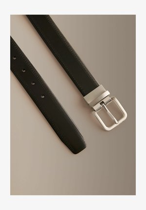 Čierny kožený opasok so striebornou obdĺžnikovou prackou a prešitými okrajmi, položený na rovine na neutrálnej béžovej ploche.