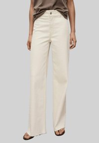 Cream wide-leg jeans made of denim, featuring a button closure, high waist, and raw hem. Paired with a relaxed-fit brown top.