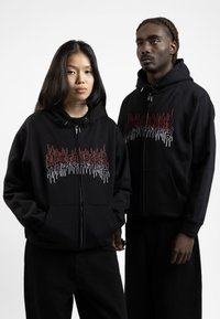 Black zip-up hoodies featuring red and white flame-style graphic designs on the front. Made of soft, textured fabric with front pockets.