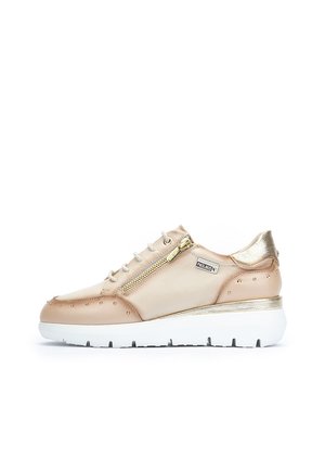 Zapatillas de cuero beige con un acabado texturizado, detalles en dorado, cremallera lateral y suela de plataforma blanca. Presenta un detalle de tachuelas en la puntera.