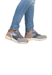 Šedé tenisky s kombinací broušené kůže a síťoviny. Mají oranžové akcenty, geometrický vzor, texturované povrchy a gumovou podrážku.