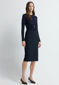 Navy niebieska bluzka z długim rękawem z skręconym przodem i metalicznym akcentem, połączona z granatową spódnicą ołówkową do kolan i czarnymi szpilkami.