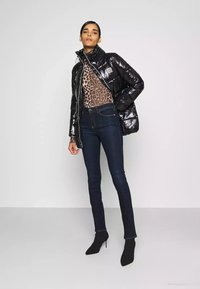 Giacca imbottita nera lucida con colletto alto, top con stampa leopardata e jeans skinny scuri. La modella indossa stivaletti neri con tacco.