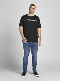 Mustat puuvillapaidat, joissa on "JACK & JONES" -logo valkoisena ja punaisena rintataskussa, yhdistettyinä sinisiin farkkuihin ja mustiin lenkkareihin.