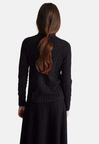 Pullover nero a coste realizzato in materiale testurizzato, con maniche lunghe e scollo rotondo, indossato sopra una gonna nera, visto da dietro.