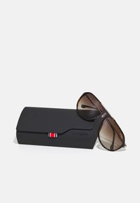 Brune gradient solbriller med skildpadde-ramme, gyldne detaljer på stængerne, sammen med et sort beskyttelsesetui med en farvet stribe og logo.