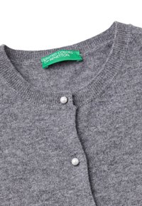 Šedý pletený kardigan s kulatým výstřihem, který má jedno bílé zapínání na knoflík a zelený značkový štítek uvnitř. Měkká textura.
