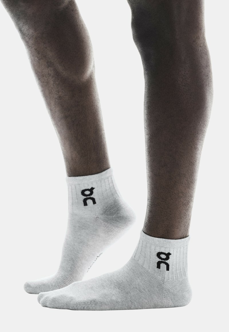 Calcetines de algodón blancos hasta el tobillo con un puño acanalado y un logotipo negro en el lateral. Textura suave, forma ajustada, diseñados para comodidad y soporte.