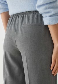 Gray tailored trousers with an elastic waistband, woven texture, and a single back pocket. Paired with a light blue sweater.