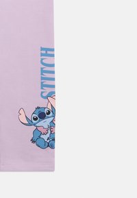 T-shirt lilla con un personaggio dei cartoni animati blu e rosa con grandi orecchie, e la parola "STITCH" in grassetto blu lungo il lato.