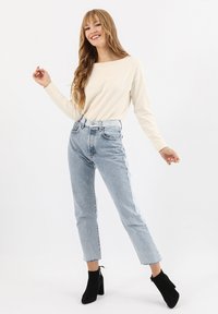 Maglietta beige chiara a maniche lunghe abbinata a jeans azzurri a vita alta, con taglio dritto e orlo sfrangiato, completata da stivali neri alla caviglia.
