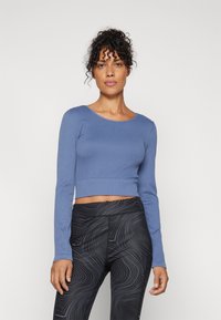 Dugi rukav svijetloplavi crop top od rebraste tkanine, uparen s crnim tajicama koje imaju uzorak valovitih linija i elastičnu pojase.