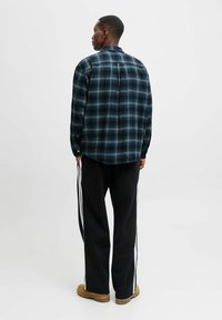 Flannel skjorte i mørkeblå og sort ternet mønster, lange ærmer, knapmanchetter, parret med sorte bukser med hvide sidestænger.