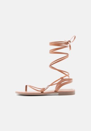 Tan lederen gladiatorsandalen met spiraalvormige enkelbandjes, platte zool en minimalistisch design. Voorzien van dunne bandjes en een lussluiting.