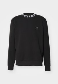 Černá mikina vyrobená z bavlněné směsi, s ribovaným límcem a textem "LACOSTE", dlouhými rukávy a malým krokodýlím logem na hrudi.