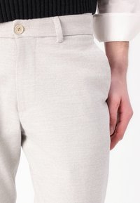 Lichtgrijze broek van gestructureerde stof, met een voorzak, riemlussen en een enkele knoopsluiting aan de taille.