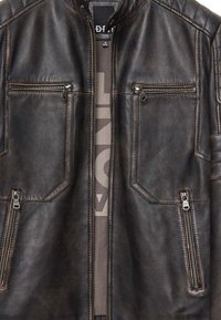 Donkerbruine leren jas met voor- en borzipvakken, centrale ritsluiting en een kleine kraag.