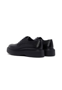 Zwarte leren schoenen met een gestructureerde afwerking, ronde neus en dikke zwarte rubberen zool. Klassiek vetersluitingsontwerp met subtiele stikseldetails.