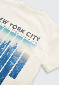 Crème katoenen T-shirt met een blauwe skyline-afbeelding van New York City en vette tekst "NEW YORK CITY" en "STAND OUT FROM THE NOISE."