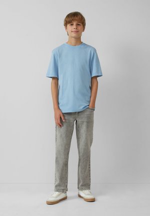  Lichtblauw katoenen t-shirt, korte mouwen, relaxte fit, gecombineerd met lichtgrijze denim jeans en witte sneakers met tan kleurige zolen.