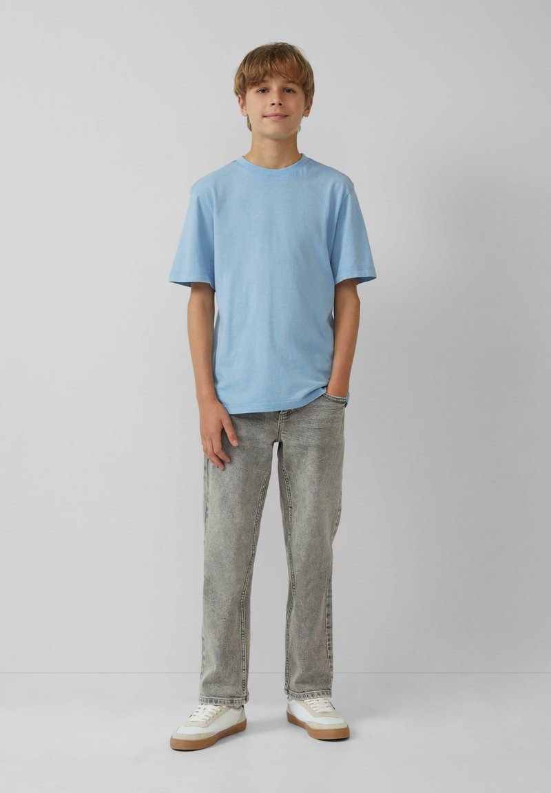 Lichtblauw katoenen t-shirt, korte mouwen, relaxte fit, gecombineerd met lichtgrijze denim jeans en witte sneakers met tan kleurige zolen.