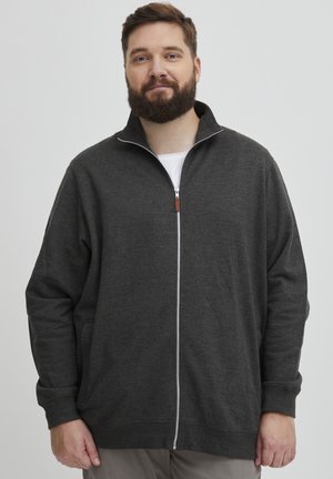 Grå zip-up hettegenser med høy krage, med en subtil tekstur, hvit glidelås og en logo-tag, brukt over en hvit skjorte.