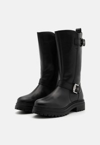 Botas de cuero negro hasta la rodilla con punta redonda, cremallera lateral y un acento de hebilla en la correa; suela de plataforma texturizada para mayor tracción.