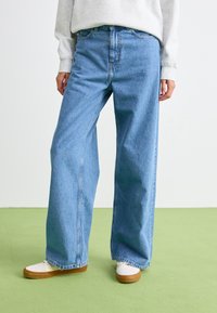 Light blue denim wide-leg jeans with a high waist, featuring a classic five-pocket design and visible seam details, paired with white shoes.
