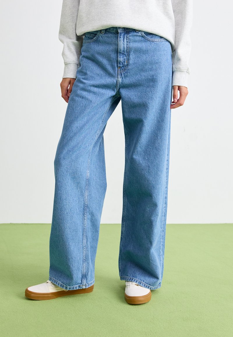 Lichtblauwe denim wijdlopende jeans met een hoge taille, voorzien van een klassiek vijf-pocket ontwerp en zichtbare naaddetails, gecombineerd met witte schoenen.