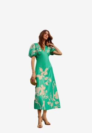 Grünes Blumen-Cocktailkleid mit Puffärmeln, V-Ausschnitt und fließender Silhouette. Verfügt über hellbeige Blumenmuster und eine elegante goldene Clutch.