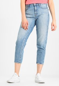 Vaaleansiniset korkeavyötäröiset farkut, joissa on kapeat lahkeet, raaka helma ja viisi taskua, yhdistettynä valkoisiin tennareihin.