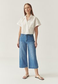 White short-sleeve shirt, light blue wide-leg jeans, and black flip-flops with white straps. Smooth fabric with a casual design.