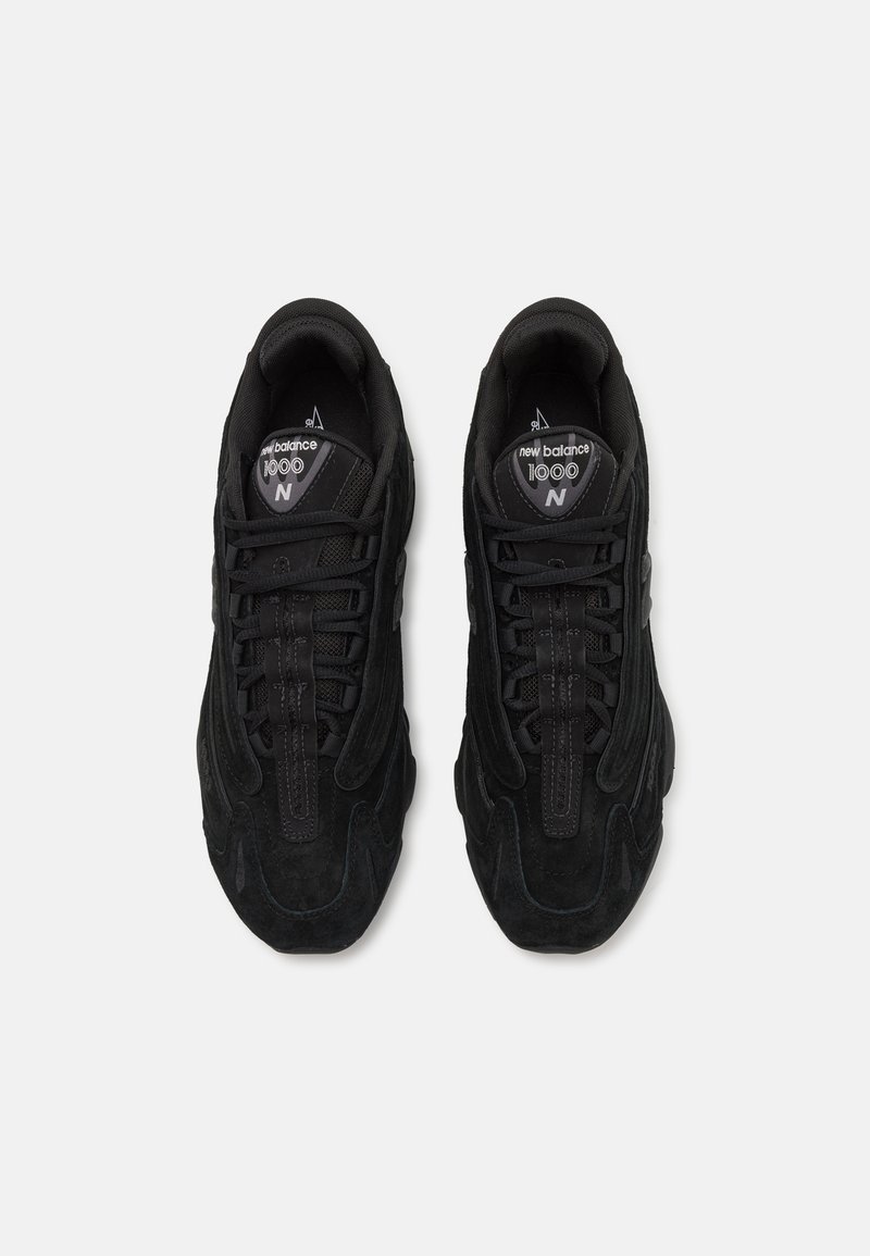 Zapatillas de ante negro con puntera redondeada, cierre de cordones y lados texturizados. Cuenta con un collar acolchado y un logotipo en la lengüeta.