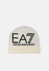 Cappello beanie in grigio chiaro, con logo nero recante il testo "EA7 Emporio Armani". Progettato con un orlo ribbed di colore crema nella parte inferiore.