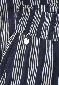Tissu rayé vertical bleu marine et blanc avec une ceinture élastique froncée et une petite plaque métallique ronde indiquant "Street One".