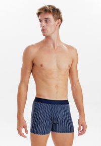 Navy boxer shorts with a white floral pattern, elastic waistband, fitted shape, and smooth fabric texture. Model shown from the side.