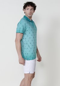 Türkiz színű pólóing, finom mintával, rövid ujjakkal és gallérral. Fehér nadrágpárral kombinálva, oldalsó díszítéssel és egy gombbal.