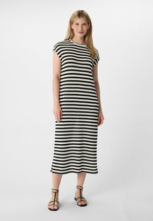 Gestreiftes Kleid in Schwarz und Weiß, knielang, mit kurzen Ärmeln, das eine weiche Stricktextur und seitliche Schlitze aufweist. Kombiniert mit schwarzen Riemchensandalen.