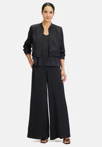 Zwarte satijnen outfit met een cropped, open voren jack met ballonmouwen, gedragen over een effen top en brede broek.