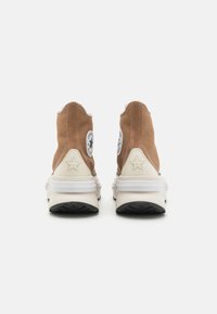 Braune Leinenschuhe mit hohem Schaft und weißen Gummisohlen, die mit einem Sternelement und Logopatches an den Seiten ausgestattet sind. Strukturierte Details an den Nähten.