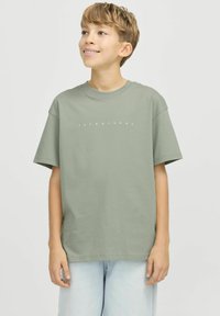 Zaļa kokvilnas T-kreklu ar apaļu kakla izgriezumu, nolaižamām plecu daļām un baltu tekstu "JACK & JONES" priekšpusē. Saskaņota ar gaiši ziliem džinsiem.