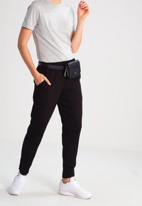 Černé joggingové kalhoty s elastickým pasem a bočními kapsami, v kombinaci se šedým tričkem s krátkým rukávem a bílými teniskami. Součástí je také černá ledvinka.