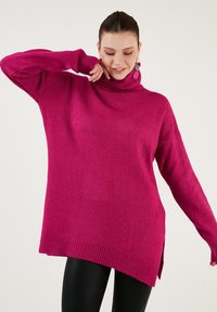 Fuksia turtleneck-paita, jossa on ribbaus hihansuissa ja helmassa, löysä istuvuus sekä sivuhalkiot lisäävät tyyliä ja mukavuutta.