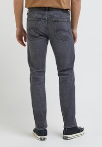 Jeans de mezclilla gris con corte ajustado, que presentan un clásico diseño de cinco bolsillos y detalles de costura sutiles. Combinados con zapatos de lona negros.