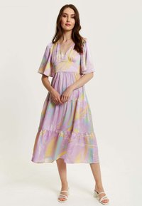 V-neck, short, flutter sleeves dress in pastel purple with abstract yellow and blue patterns; tiered, flowing design and lightweight fabric.