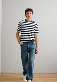 Gestreiftes navy und weißes T-Shirt mit kurzen Ärmeln und Rundhalsausschnitt, kombiniert mit hellblauen Jeans und weißen Sneakers.