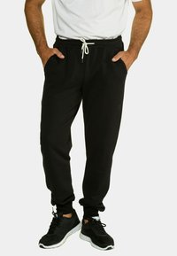 Schwarze Jogginghose mit elastischem Bund und Kordelzug, ausgestattet mit Seitentaschen und schmal zulaufenden Bündchen, kombiniert mit schwarzen Sportschuhen.
