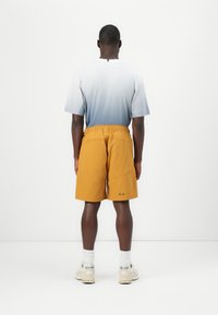 Men’s outfit featuring a light blue gradient t-shirt and mustard yellow shorts with an elastic waistband and pocket details. Sneakers included.
